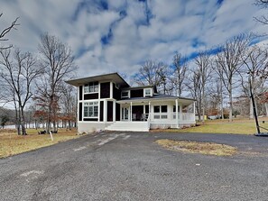 A two-story house with a porch, a driveway, and a wooded area in the background. - Starlit Memories by Taylor Made Deep Creek (Swanton)