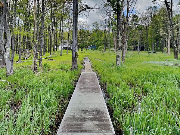 A wooden pathway leading to a house surrounded by tall trees and lush green grass. - Starlit Memories by Taylor Made Deep Creek (Swanton)
