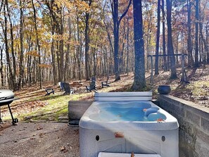 A hot tub in a forested area with chairs and a picnic table.