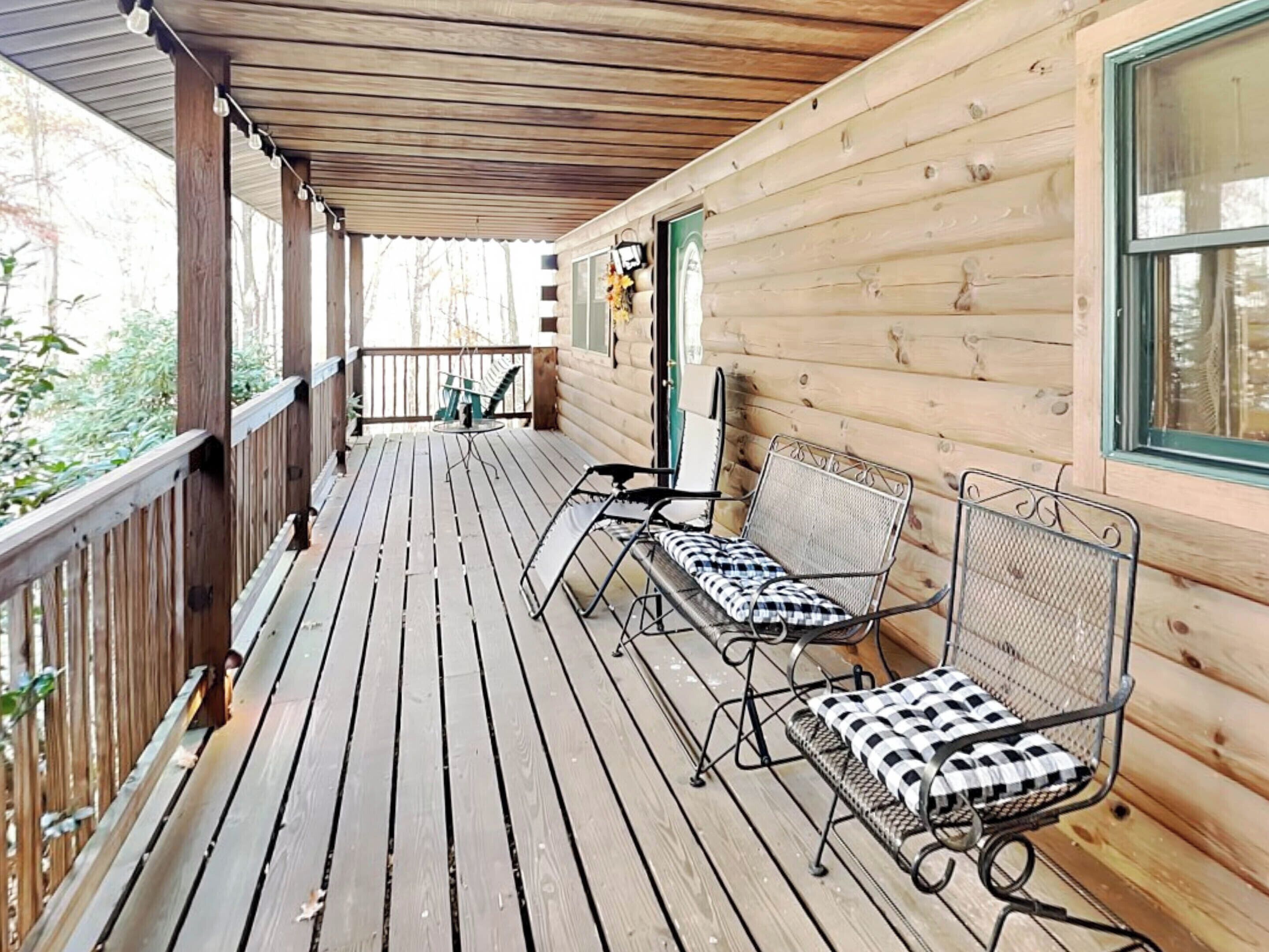 Una terraza de madera con dos sillas de metal y un banco, baranda de madera y vistas del entorno.