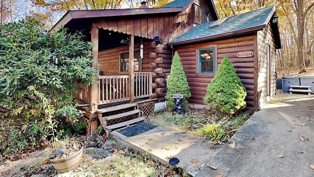 A rustic log cabin with a porch, two evergreen trees, and a welcome sign. - Cozy Cabin by Taylor Made Deep Creek (Oakland)