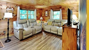 A cozy cabin interior with a wooden ceiling, two leather sofas, a small table, and a television on a wooden stand. - Cozy Cabin by Taylor Made Deep Creek (Oakland)