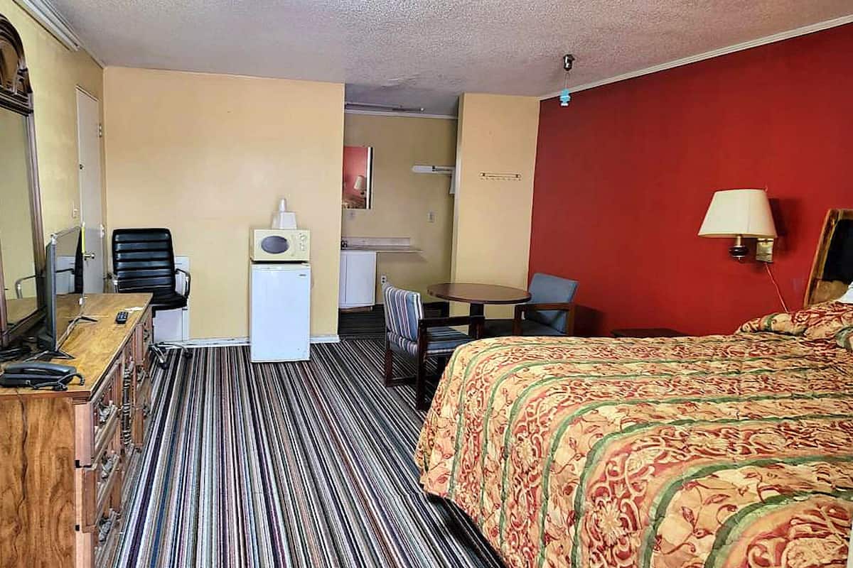 A hotel room with a bed, a desk with a telephone, a chair, a small table, and a lamp.