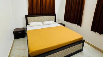 A hotel room with a bed, curtains, an air conditioning unit, and a nightstand.