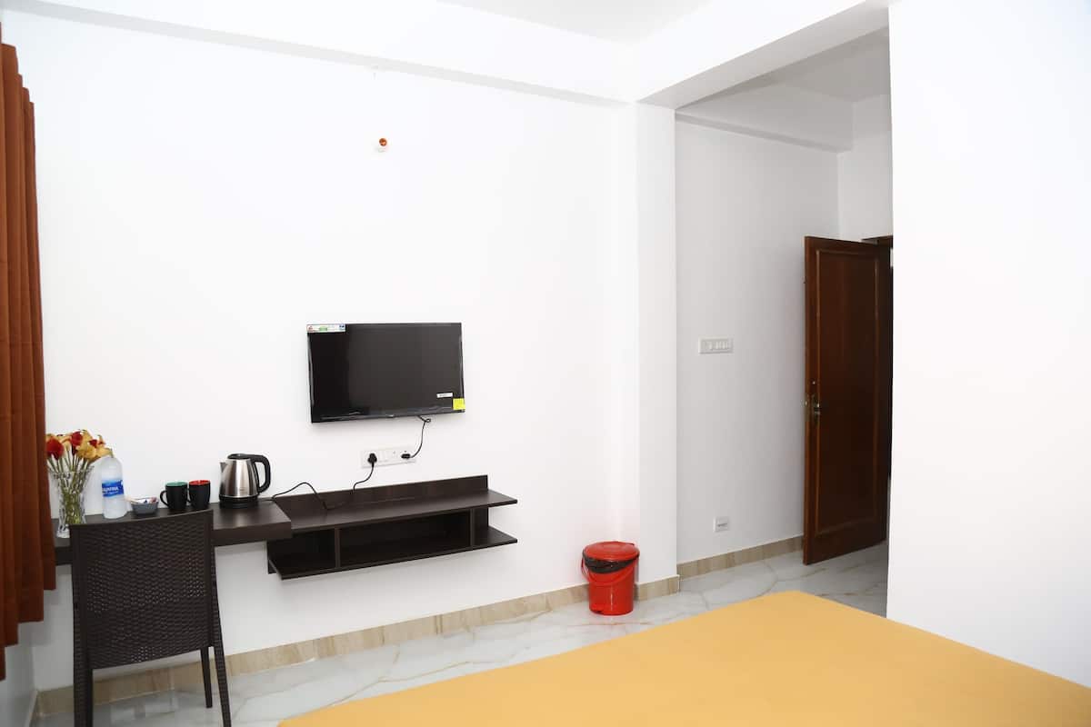 A room with a TV mounted on the wall, a small table with a kettle, a red bucket, and a chair.