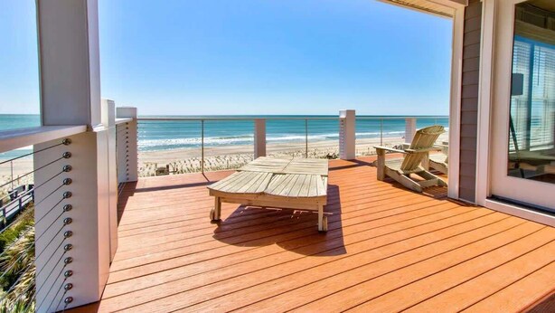 Une terrasse en bois avec un fauteuil de relaxation et deux chaises Adirondack donnant sur une plage.