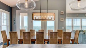 Un espace repas avec une table en marbre, des chaises en osier et une vue sur l’océan.