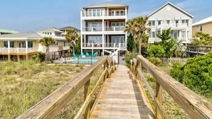 Un hôtel de plusieurs étages situé en bord de mer, avec une promenade en bois menant à l’entrée.