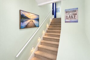 A staircase with carpeted steps, a painting of a lake, and a welcome sign. - Lake George Village• By Lake, Beach & Ski Slopes. Gore & West Mountains nearby. (Lake George)