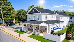A two-story house with a porch, number 95, and a covered outdoor seating area with a grill. - Lake George Village -1 Block to Beach, Lake, Town. Newly Remodeled and Spacious. (Lake George)