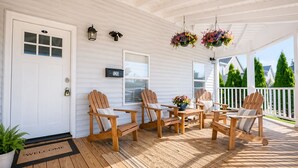 A covered porch with wooden chairs, a welcome mat, and hanging flower baskets. - Lake George Village -1 Block to Beach, Lake, Town. Newly Remodeled and Spacious. (Lake George)