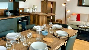 A modern kitchen with a wooden countertop, built-in oven, and a dining area set for six with plates, glasses, and cutlery. - L'Éclat Champenois - Gare/Arena (Reims)