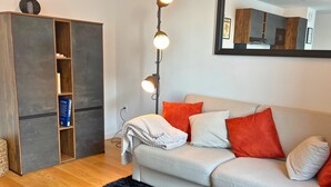 A living room with a sofa, pillows, a bookshelf, and a floor lamp. - L'Éclat Champenois - Gare/Arena (Reims)