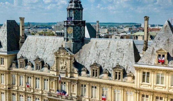 Un edificio histórico con arquitectura clásica, que destaca por una torre de reloj prominente y múltiples banderas.