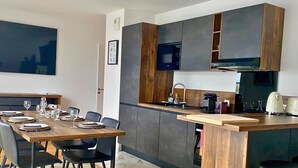 A modern kitchen with dark cabinetry, a wooden island, and a dining area with a table set for four. - L'Éclat Champenois - Gare/Arena (Reims)