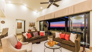 A modern living room with two sofas, a coffee table, and a ceiling fan. There is a large window with a view of the sunset. - Scenic Views Diamante 2Bdr Condo DRC #306 (Cabo San Lucas)