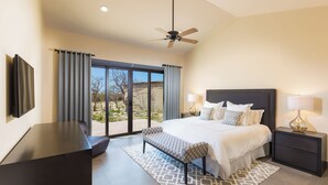 Un dormitorio con cama, mesitas de noche, escritorio, banco, ventilador de techo y vistas al exterior.