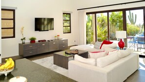 Una sala de estar moderna con un sofá, una mesa de centro y un televisor montado en la pared. Se ve un ventanal con vista a la vegetación.