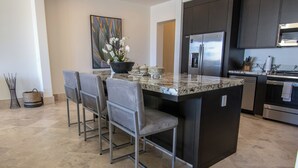 A modern kitchen with a granite island, stainless steel appliances, and a seating area with chairs.