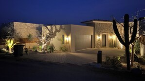 A modern house with a stone facade, a garage, and a well-lit driveway at night.