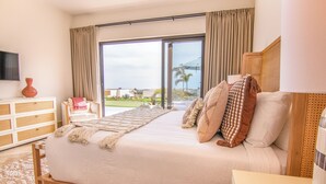 Un dormitorio con una cama grande, televisión, cómoda de madera y vistas al exterior a través de una puerta corrediza de vidrio.