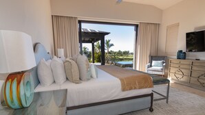 A bedroom with a large bed, a television, a desk with a lamp, and a view of a pool and palm trees. - Luxurious Golf Villa #59 – 5-Bedroom (Cabo San Lucas)
