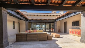 A covered outdoor seating area with wicker furniture and a stone floor. - Luxurious Golf Villa #59 – 5-Bedroom (Cabo San Lucas)