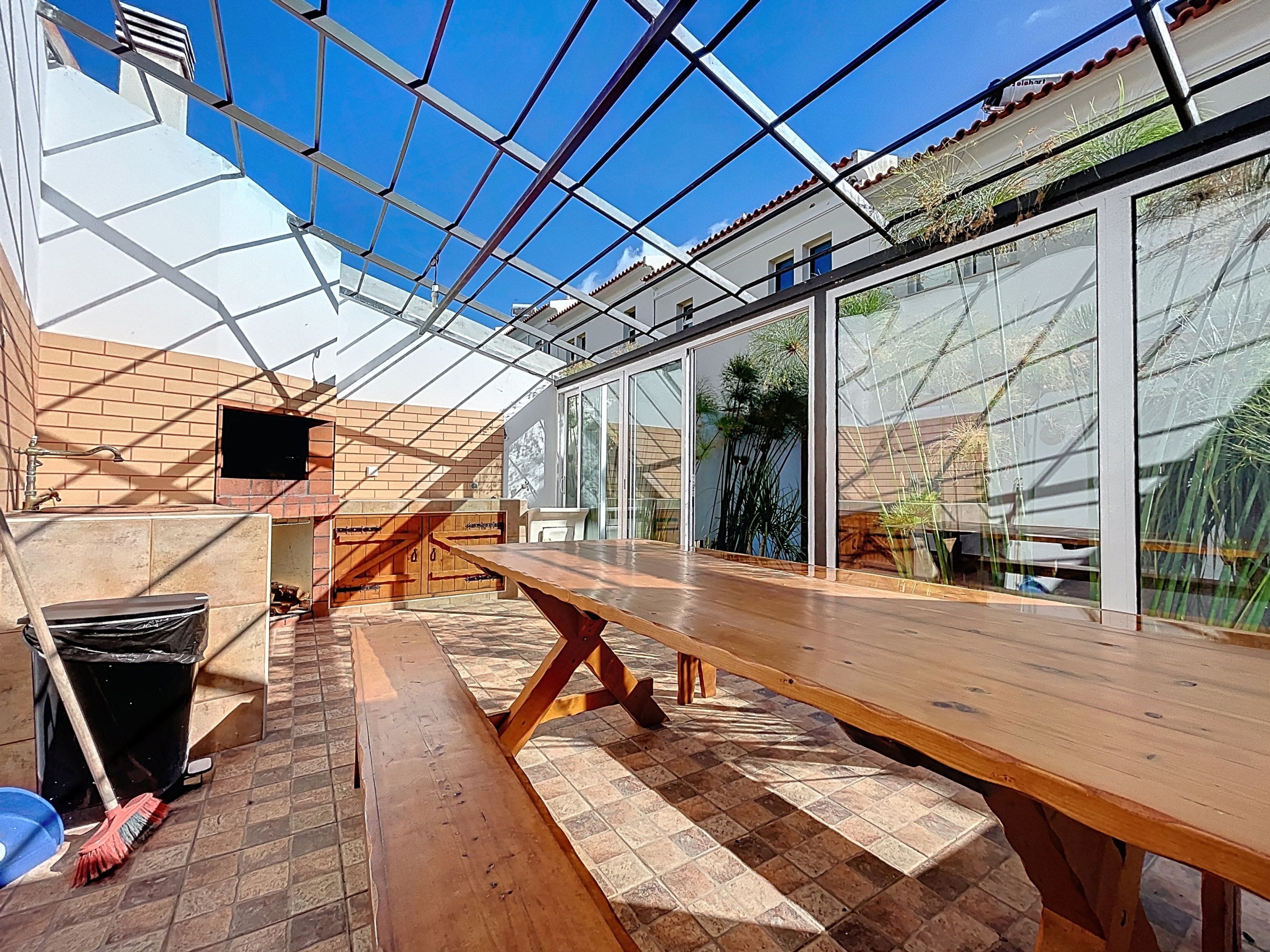 Een zonnehuis met een houten bankje, een bakstenen muur en een groot raam.