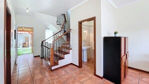 A spacious hallway with a wooden staircase leading to a second floor, a tiled floor, and a door leading to a bathroom. - Eddys House by Atlantic Holiday (Machico)