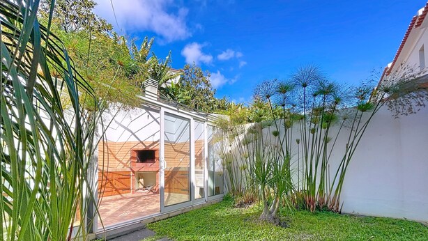 A modern house with a glass-enclosed patio, a brick fireplace, and a well-maintained garden with stone pathways. - Eddys House by Atlantic Holiday (Machico)