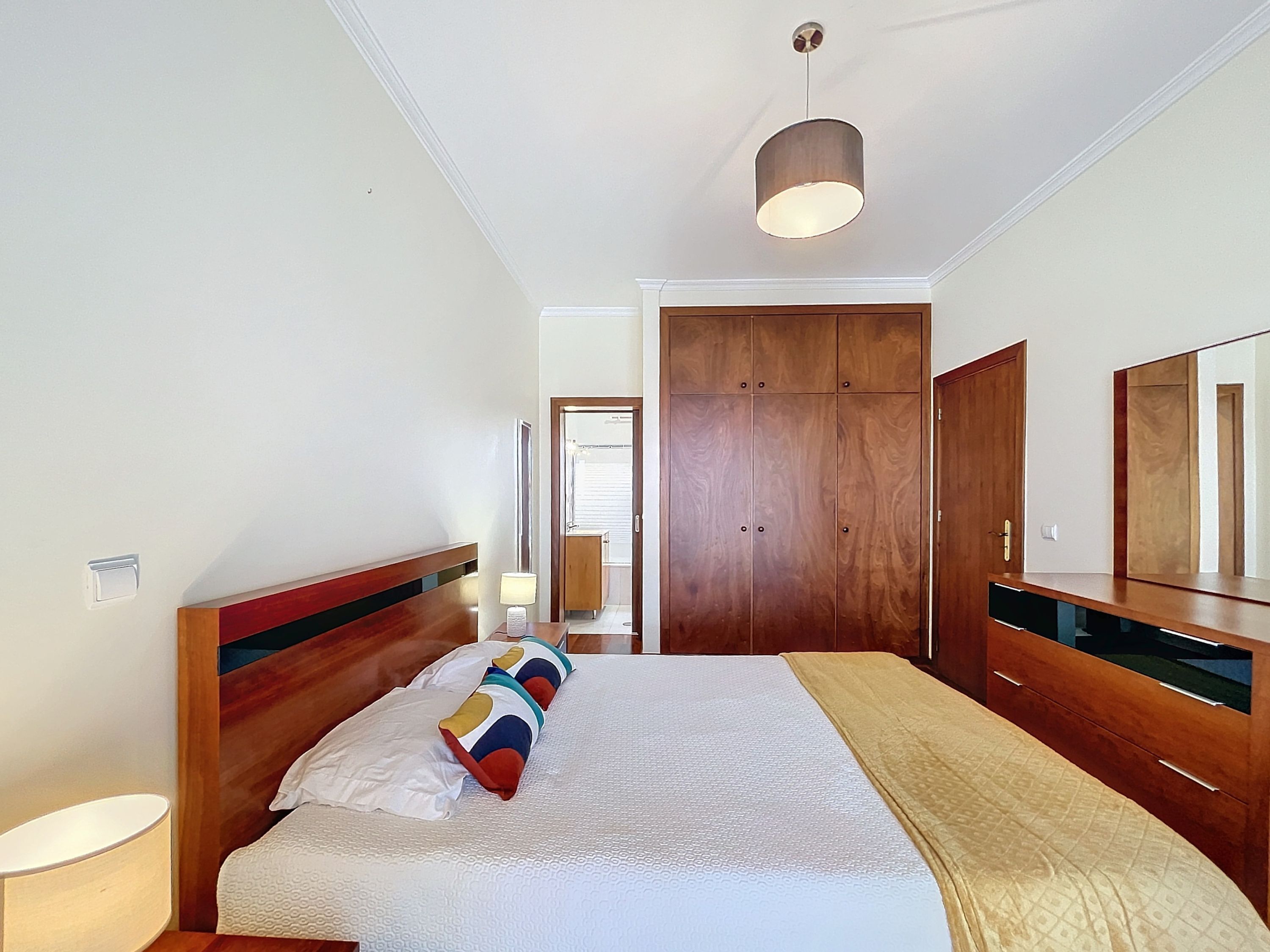 Une chambre à coucher avec un lit, une lampe de chevet, une armoire et un miroir.