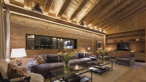 A modern living room with a wooden ceiling, a large flat-screen TV, and a fireplace. - Alpine Luxury Chalet Konk in Switzerland (Zermatt)
