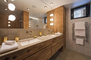 A modern bathroom with two sinks, wooden cabinetry, a large mirror, and a towel rack. - Alpine Luxury Chalet Konk in Switzerland (Zermatt)