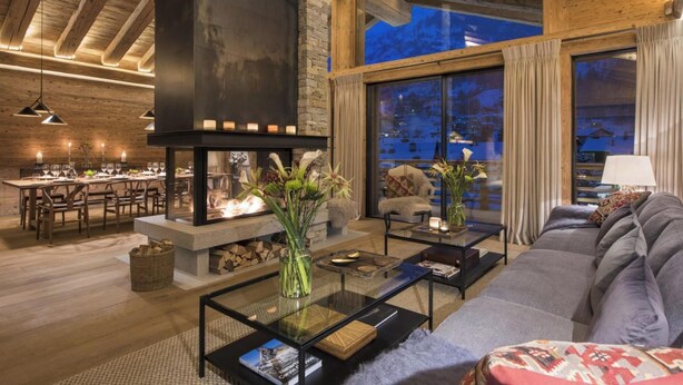 A cozy living room with a fireplace, a dining area, and a large window with a view of the outside. - Alpine Luxury Chalet Konk in Switzerland (Zermatt)