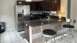 Una cocina moderna con armarios de madera oscura, electrodomésticos de acero inoxidable, una encimera de granito y dos taburetes de bar.