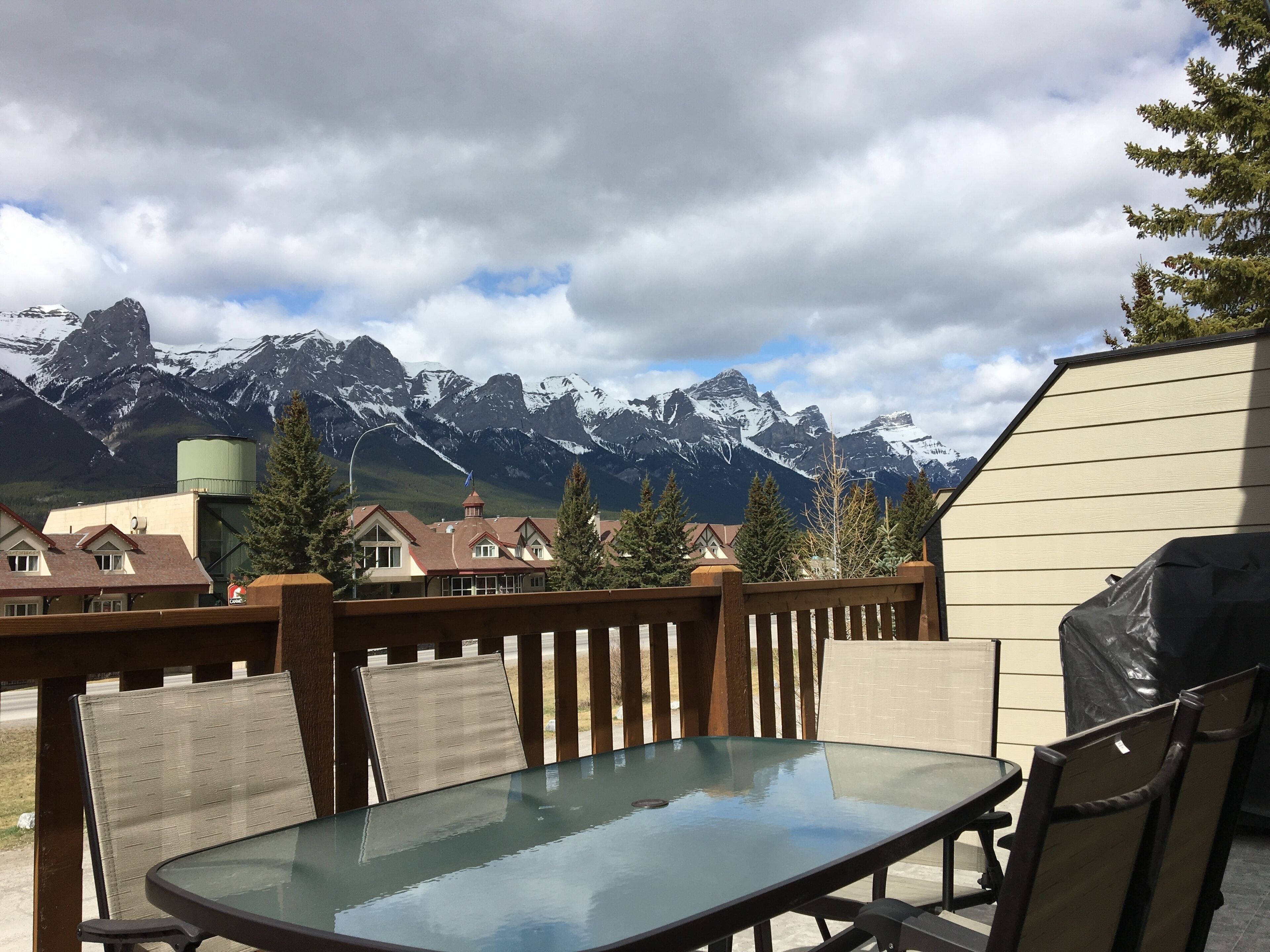 Une terrasse avec une table et des chaises en verre, offrant une vue sur une chaîne de montagnes aux sommets enneigés.