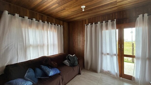 A room with a wooden ceiling, a brown sofa with blue cushions, a backpack on the sofa, and a door leading outside.
