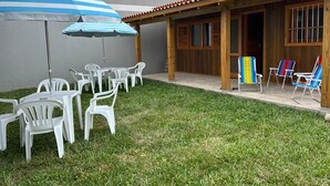A patio area with white plastic chairs and tables, a striped umbrella, and colorful beach chairs.