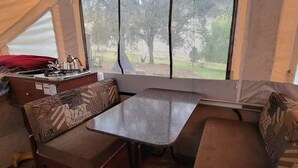 Ein kompaktes Wohnmobil-Interieur mit einer Küchenzeile, einer Essecke und einem großen Fenster mit Blick auf ein bewaldetes Gebiet.