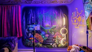 Una habitación con un mural llamativo, una cámara sobre un trípode y una cortina morada.