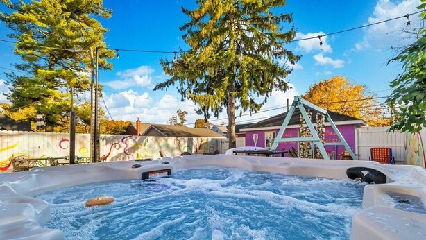 Un jacuzzi en un patio trasero con terraza de madera, un edificio morado y árboles.