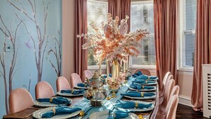 Comedor con una larga mesa dispuesta para una comida, decorada con centros de mesa florales y elegantes vajillas.
