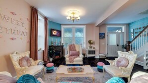 Una sala de estar acogedora con chimenea, dos sillones, una mesita de centro y una escalera con barandilla azul.