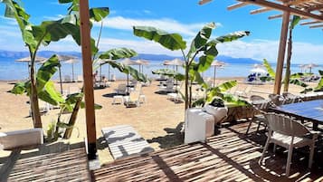 A beachside patio with wooden flooring, thatched roof structures, and outdoor seating.