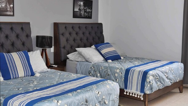 Une chambre d’hôtel avec deux lits, chacun doté d’une tête de lit capitonnée, d’une table de chevet avec une lampe et de tableaux encadrés accrochés au mur.