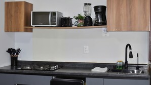 Une cuisine équipée d’un four à micro-ondes, d’une machine à café, d’un mixeur et d’une étagère sur laquelle est posée une plante.