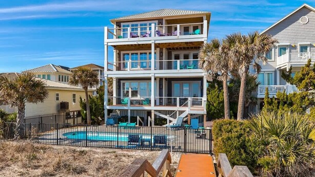 Une propriété en bord de mer, composée de plusieurs étages, dotée d’une piscine, d’un espace extérieur aménagé et de palmiers.