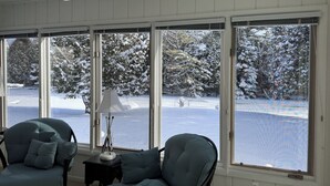 Ein Zimmer mit Blick auf eine verschneite Landschaft durch große Fenster, einem Deckenventilator und zwei mit Kissen ausgestatteten Stühlen.
