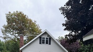 Ein zweistöckiges Haus mit weißer Fassade, einer roten Haustür und einem kleinen Vorbau mit weißem Geländer.