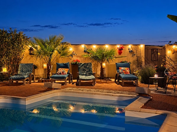 A poolside area with lounge chairs, a swimming pool, and decorative lighting.
